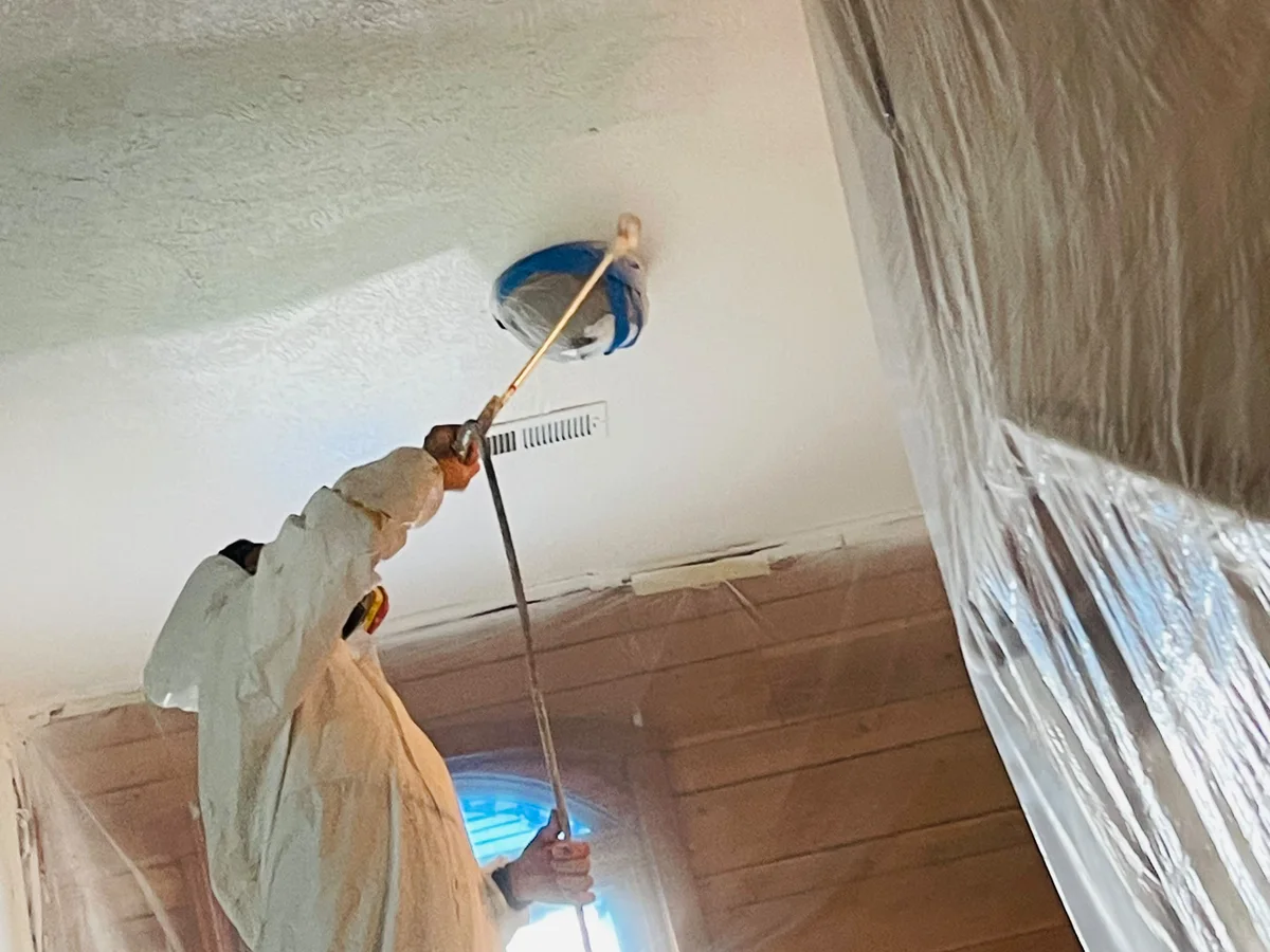 Painter rolling a ceiling with the room covered